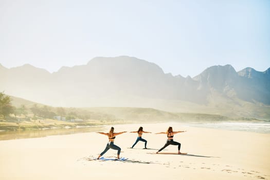 Be a warrior not a worrier. three young women practicing yoga on the beach