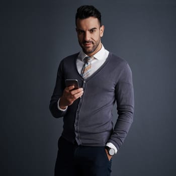 Availability is the key to my success. Studio shot of a stylish young businessman using a mobile phone against a gray background