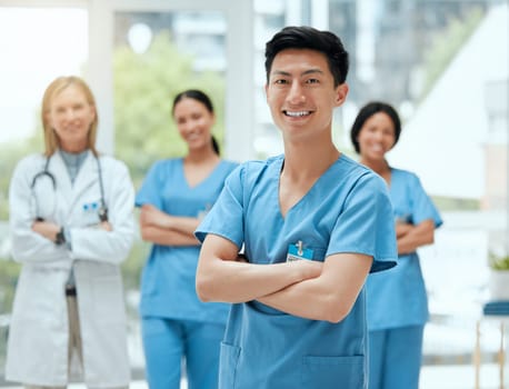 Portrait, medical and an asian man nurse arms crossed, standing with his team in a hospital for healthcare. Leadership, medicine and teamwork with a male health professional in a clinic for treatment.