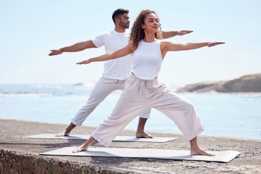 Couple yoga, beach and exercise outdoor in nature for fitness workout and wellness. African woman and a man at ocean for warrior pose, stretching or pilates training for peace, freedom or mindfulness.