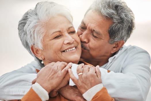 Happy elderly couple, hug and sunset with kiss on cheek, bonding and smile for romance, love and vacation. Senior man, woman and embrace with happiness, retirement and travel together for holiday.
