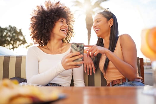 Laughing, happy and women with a phone at a cafe for a meme or social media notification. Smile, talking and friends with a mobile for a funny app, comic conversation or comedy together at restaurant.