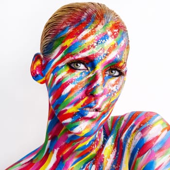 Studio shot of a young woman posing with brightly colored paint on her face against a white background.