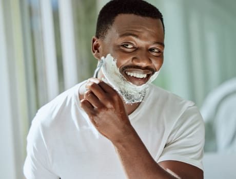 Cream, razor and shaving black man in the bathroom for skincare, beard grooming routine and facial care. Smile, treatment and African person start to shave face for hair removal with foam in morning.