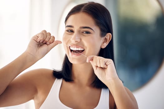 Smile, woman in bathroom flossing teeth and morning dental care routine in home mirror. Health, wellness and Indian woman with dental floss, motivation for cleaning for healthy mouth and fresh breath.