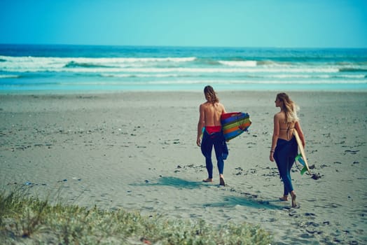 Get on your board and surf. a young couple walking on the beach with their surfboards