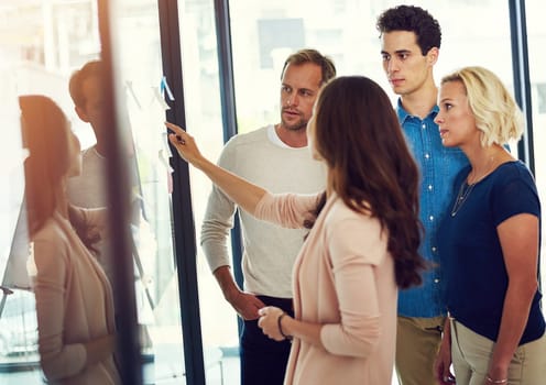 Focused on taking the steps to make it big. a group of young designers brainstorming with notes on a glass wall in an office