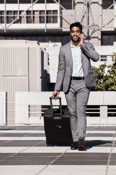 Phone call, travel and luggage with a businessman walking in the city for a company trip. Mobile, communication or suitcase with a young male employee talking while on a commute outdoor in town.