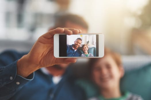 This is a good picture of us. Closeup of a cheerful little boy and his father taking a self portrait together while being seated on the sofa together