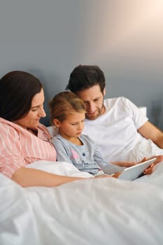 Find out what your kids love watching. a young family using a tablet while chilling in bed together at home
