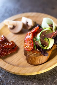 close-up of black bread bruschetta with tomato and cucumber on a wooden plate.