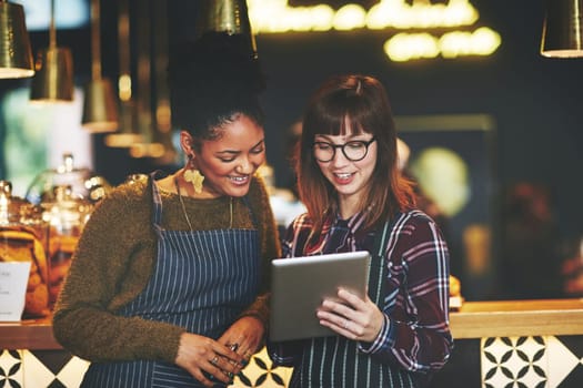 Marketing their cafe using good old social media. two young women using a digital tablet together while working at a coffee shop