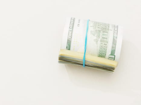 A stack of one hundred dollar bills tied with a blue rubber band on a white background top view.