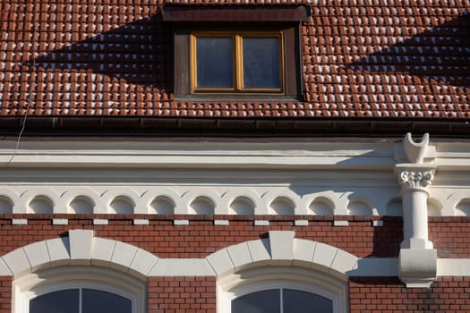 A small section of the historic building in close-up. Front view of the roof dormer and ornate cornice and a piece of the red brick facade.
