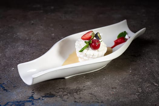 white dessert fresh meringue with strawberries on a beautiful white dish on a dark background.