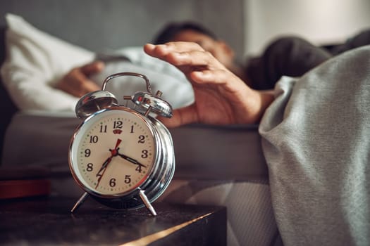 Alarm clock, wake up and man sleeping in the bedroom of his modern apartment in the morning. Lazy, resting and hand of male person taking a nap and dreaming in bed with time watch at his home