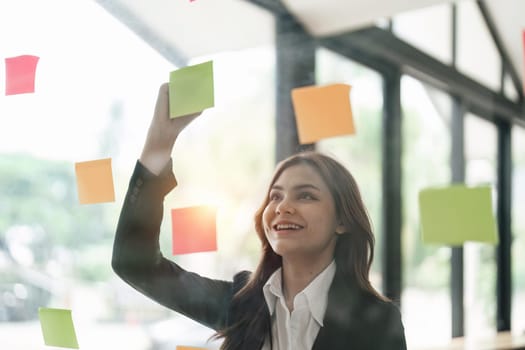 Asian businesswoman creating project plan on office wall with paper notes. Financial and Marketing projects.