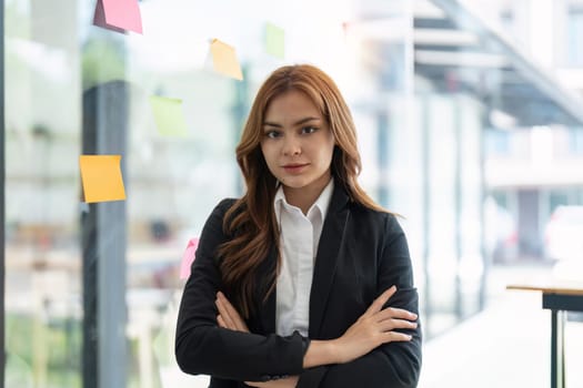 Portrait young confident Asian business woman leader, successful entrepreneur, elegant professional company executive ceo manager, wearing suit standing in office with arms crossed in meeting room.