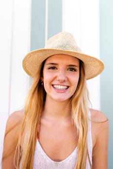 Headshot of young happy blond woman on vacation wearing hat looking at camera. Vertical portrait.