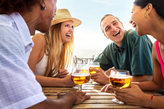 Group of multiracial young friends laughing having fun at beach bar drinking beers together. Friends on summer vacation. Lifestyle concept.