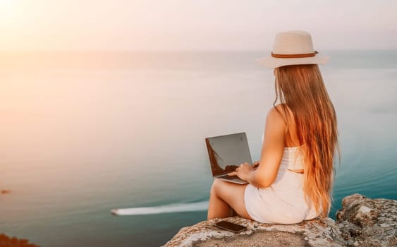 Digital nomad, Business woman working on laptop by the sea. Pretty lady typing on computer by the sea at sunset, makes a business transaction online from a distance. Freelance, remote work on vacation