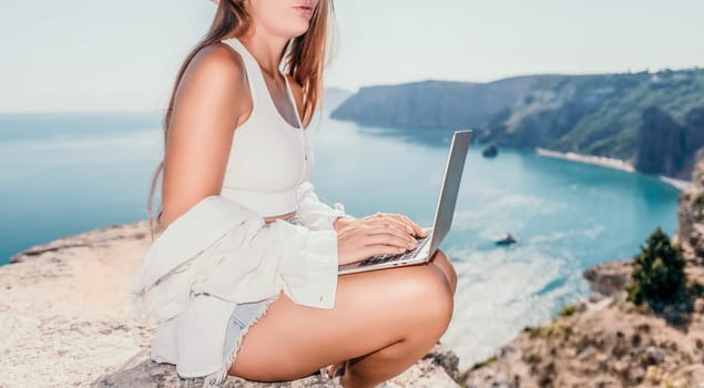 Digital nomad, Business woman working on laptop by the sea. Pretty lady typing on computer by the sea at sunset, makes a business transaction online from a distance. Freelance remote work on vacation