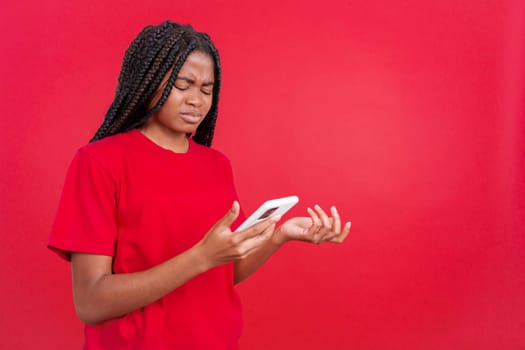 Worried african woman using a mobile phone in studio with red background