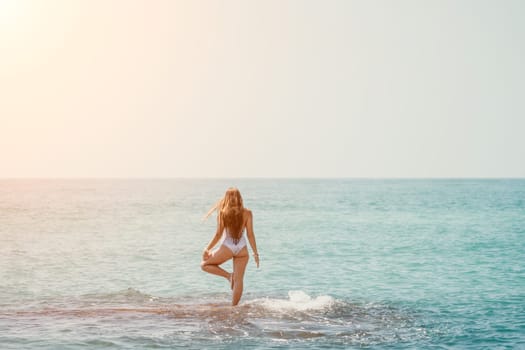 Woman sea yoga. Back view of free calm happy satisfied woman with long hair standing on top rock with yoga position against of sky by the sea. Healthy lifestyle outdoors in nature, fitness concept.