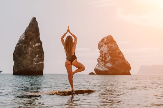 Woman meditating in yoga pose silhouette at the ocean, beach and rock mountains. Motivation and inspirational fit and exercising. Healthy lifestyle outdoors in nature, fitness concept.