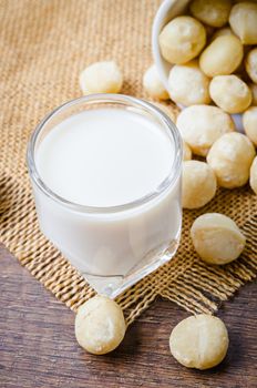 Macadamia milk in a glass and a bowl of macadamia nuts on a wooden background.