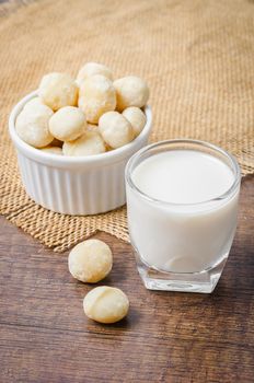 Macadamia milk in a glass and a bowl of macadamia nuts on a wooden background.