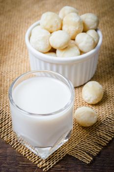 Macadamia milk in a glass and a bowl of macadamia nuts on a wooden background.