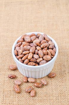 Raw Organic cranberry beans in white cup on sack background.