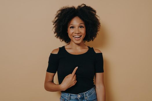 Young mean me? Portrait of happy young mixed race woman pointing finger at herself and looking at camera with amazed face expression, dressed in black t shirt. Body language and human emotions