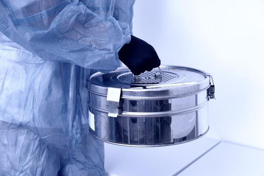 A Person standing in Laboratory holding Autoclave Sterilizer metal box wearing protective uniform