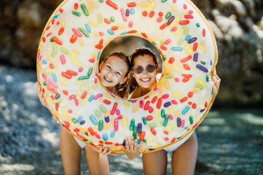 A beautiful teenage girl and her young mother having fun and looking through inflatable rubber circle on the beach. 