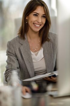 An attractive business woman checking something out of a notebook while using a computer.