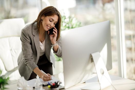 A successful business woman talking on smartphone while working at desk in her home office.