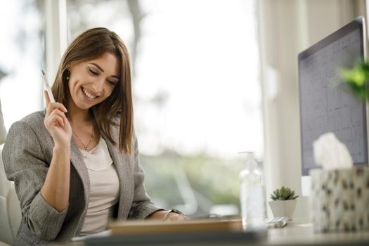 A cheerful business woman checking something out of a notebook while working in her home office.