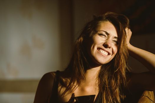 A young happy woman pensive sitting, relaxing and enjoying a sunny morning in the room.