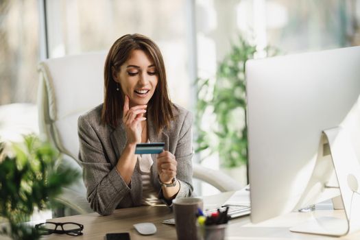 An attractive young business woman using a computer and credit card in the office.