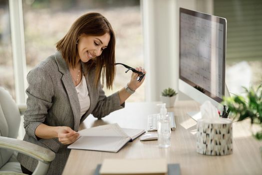 An attractive smiling business woman checking something out of a notebook while working in her home office.