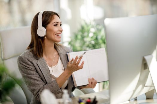 A smiling young woman using a computer to have a web conference at home office.