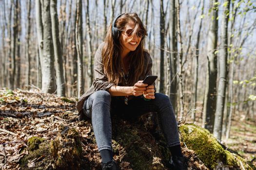 A smiling young woman using her smartphone and listening music while enjoying in nature.