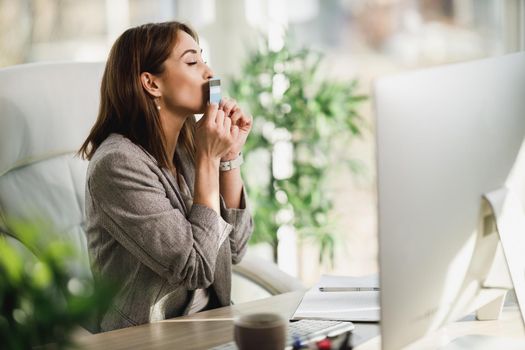 An attractive young business woman kissing her credit card while shopping online in the office.