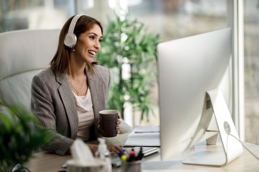 A smiling business woman enjoying a cup of coffee while working on computer at the home office.