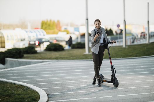 A young businesswoman using her smartphone and going to work with an electric push scooter .