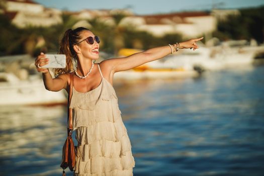 Shot of a young woman making video call with her smartphone while exploring the wonderful seaside of Mediterranean.