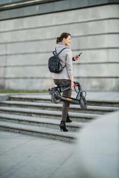 Shot of a young businesswoman using a smartphone while traveling with an electric scooter through the city.