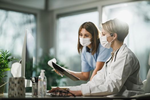 Afemale doctor and young nurse working together on computer in consulting room in the hospital.